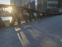 a person riding a skate board across a bridge in the sun light with buildings in the background