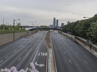 the large empty road goes over some bushes and tall buildings on either side of it