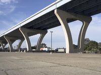 a large cement freeway bridge with multiple ramps and buildings in background as seen from a parking lot