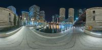 a night shot with large circular walkway along waterfront and city skyline in background at night time