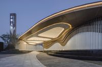 the entrance to a modern, curved building at night with lights from below the roof