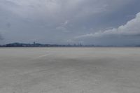 the large white airplane is traveling on the empty ground of an airport runway with a city skyline in the distance