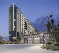 a large hotel with many windows lit up in the evening and at night near a parking lot