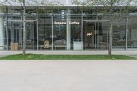 a sign and bench outside a large building with glass walls and grass in front of it