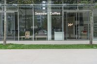 a sign and bench outside a large building with glass walls and grass in front of it