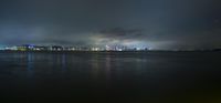 a cloudy sky with light shining over a cityscape at night from the water