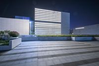 a very tall building with some lights in the background is illuminated from underneath it and sits along an empty floor in a plaza