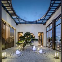 several lanterns in a courtyard with tree at the entrance of a building in china as seen on a twilight evening