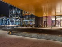 an illuminated shopping mall at night with people sitting outside and on benches to the side