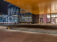 an illuminated shopping mall at night with people sitting outside and on benches to the side