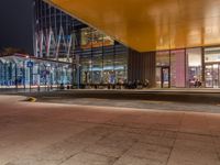 an illuminated shopping mall at night with people sitting outside and on benches to the side