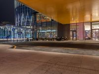 an illuminated shopping mall at night with people sitting outside and on benches to the side