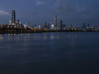 a long blue lake sits in front of a large cityscape at night with tall buildings