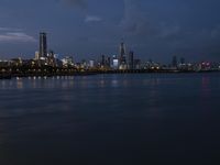 a long blue lake sits in front of a large cityscape at night with tall buildings