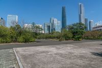 an empty parking lot and large city skylines in the background, with a small road running towards the ground and trees lining the edges