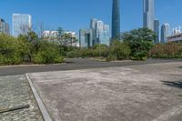 an empty parking lot and large city skylines in the background, with a small road running towards the ground and trees lining the edges