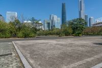 an empty parking lot and large city skylines in the background, with a small road running towards the ground and trees lining the edges