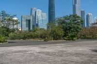 an empty parking lot and large city skylines in the background, with a small road running towards the ground and trees lining the edges