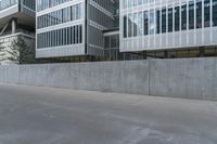 concrete wall next to buildings with glass windows next to a sidewalk in city setting with skateboard on it