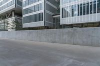 concrete wall next to buildings with glass windows next to a sidewalk in city setting with skateboard on it