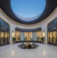 an indoor courtyard with fountain and glass doors, with round water feature in center, is surrounded by a glass wall