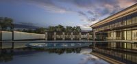 a swimming pool at the side of a building with sky reflected off it and trees in front