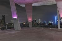 a large concrete structure with purple light in it's center in the middle of the city