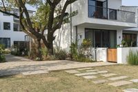 a white home is in the middle of the grassy area on the lawn, near the front of it there are plants and a tree