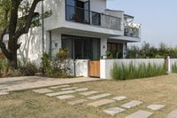 a white home is in the middle of the grassy area on the lawn, near the front of it there are plants and a tree