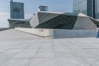 two people walk together in front of a large building that has a geometric design on the front of it