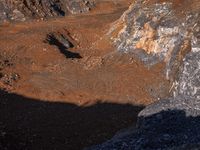 an eagle flies by some rock in the air above a muddy area in an arid mountain