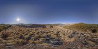 a view over the desert with sun in sky and mountain in foreground as seen through a round lens