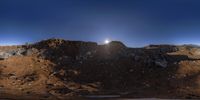 a big bright light shines above a rocky hill with a sky background at dusk