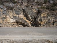 a motorcycle is parked on the side of the road beside a mountain cliff with vegetation on the edge