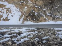 the road near a rock and snowy mountain is covered with snow and rocks, and there are no cars in sight