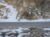 the road near a rock and snowy mountain is covered with snow and rocks, and there are no cars in sight