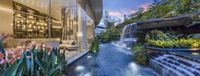 an outdoor waterfall is flowing in the garden to a house with glass walls and wood flooring