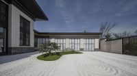 a house with a long graveled patio has two trees and grass in the middle of it