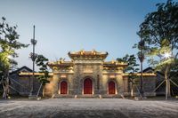 the front entrance to a temple in front of trees and sky, with bright lights on