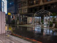 an outside restaurant on a rainy day with a neon sign, lights and benches in the rain