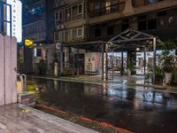 an outside restaurant on a rainy day with a neon sign, lights and benches in the rain