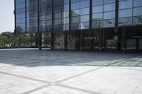 empty open space outside a very large building with large glass windows and a person walking in the courtyard