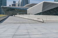 man skateboarding on a paved walkway leading to a large building with a sloping, geometric pattern