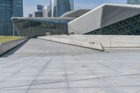 man skateboarding on a paved walkway leading to a large building with a sloping, geometric pattern