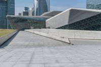 man skateboarding on a paved walkway leading to a large building with a sloping, geometric pattern