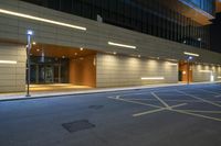 an empty city street at night next to a tall building that has lights on and two doors