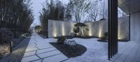 a white garden at night with a grey wall and stone walkway in front of it