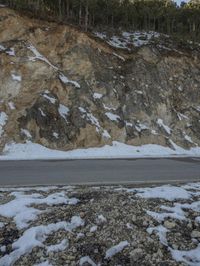 a car driving through the snow on a road side next to a cliff covered in snow