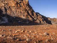 a person on a dirt trail walking by a steep, rocky cliff side near water