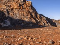 a person on a dirt trail walking by a steep, rocky cliff side near water